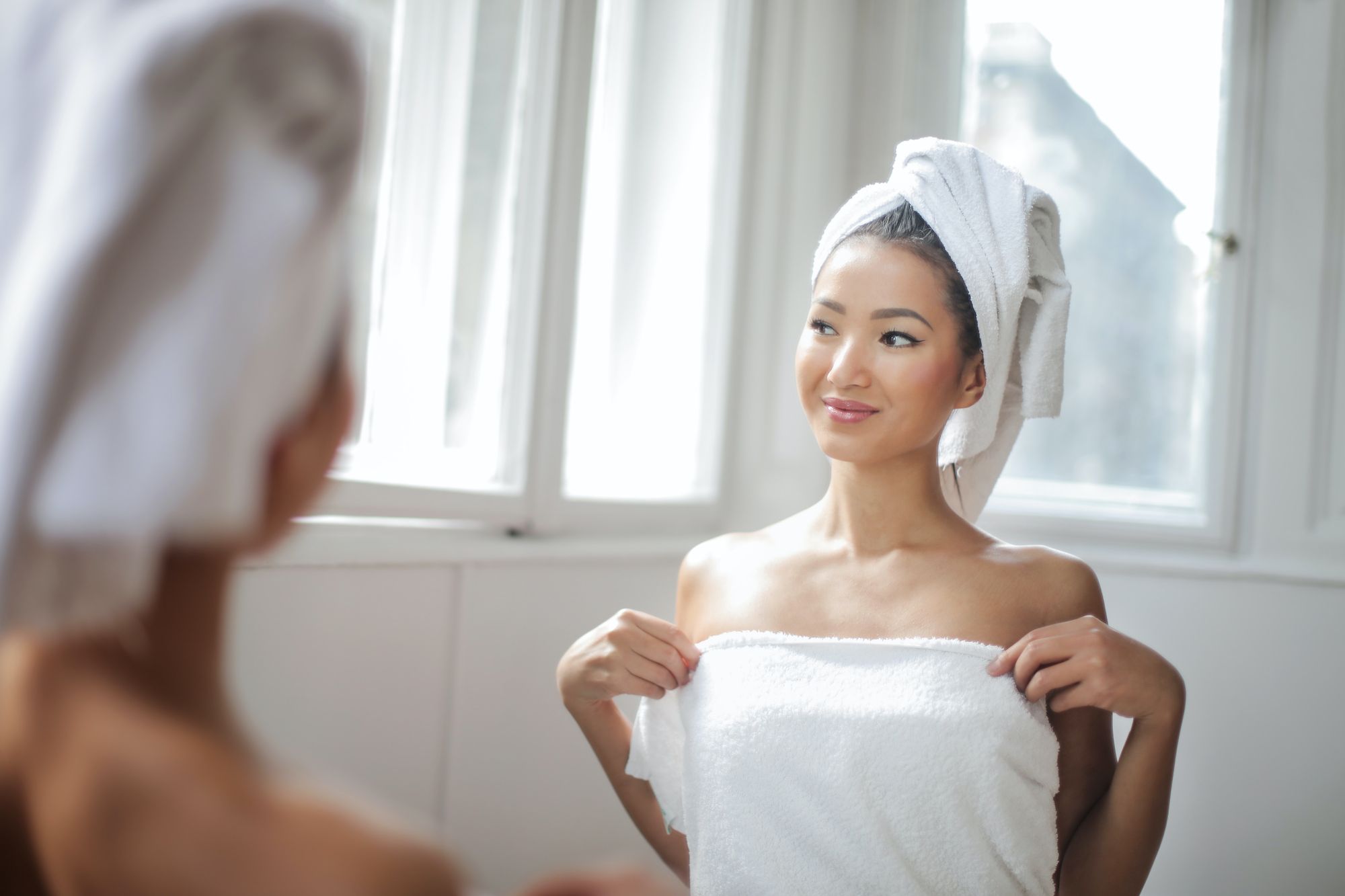 Woman in white towel about to do a breast self-exam.